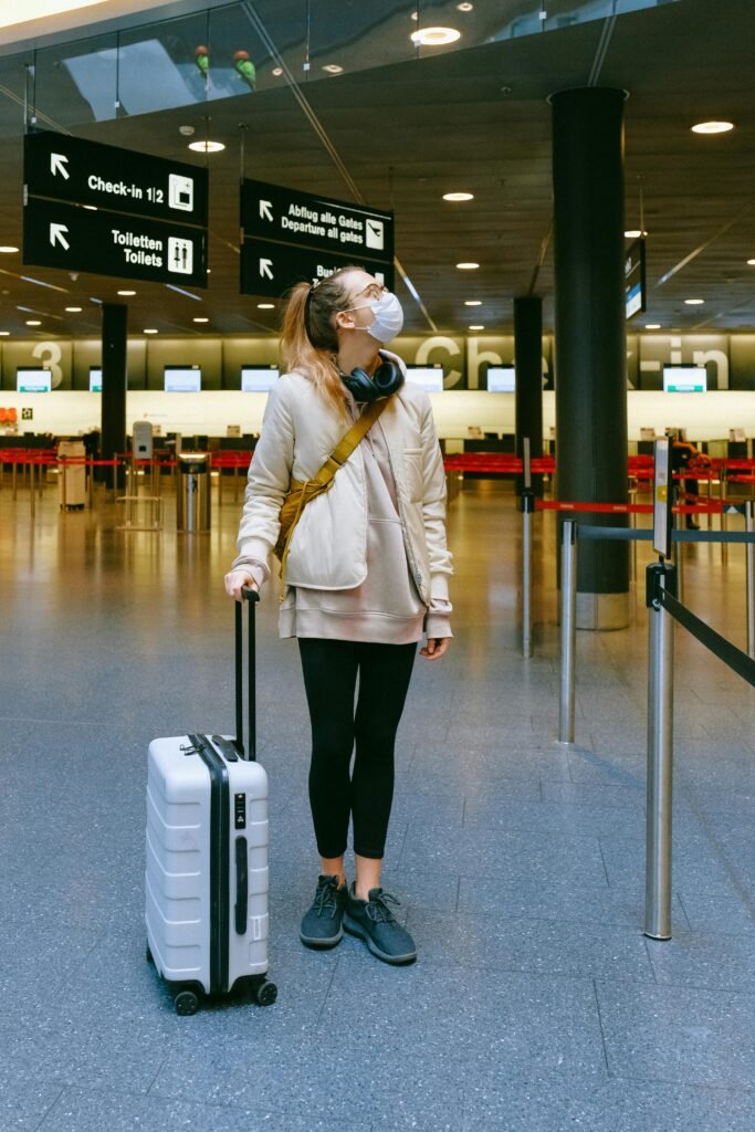 A woman in a face mask stands with her luggage in an empty airport terminal.