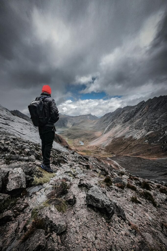 A lone hiker stands on rocky terrain overlooking a stunning mountainous landscape in Oyón, Perú.